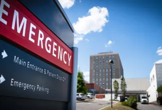 Exterior view of a hospital emergency entrance sign with directional arrows for patient drop-off and parking.